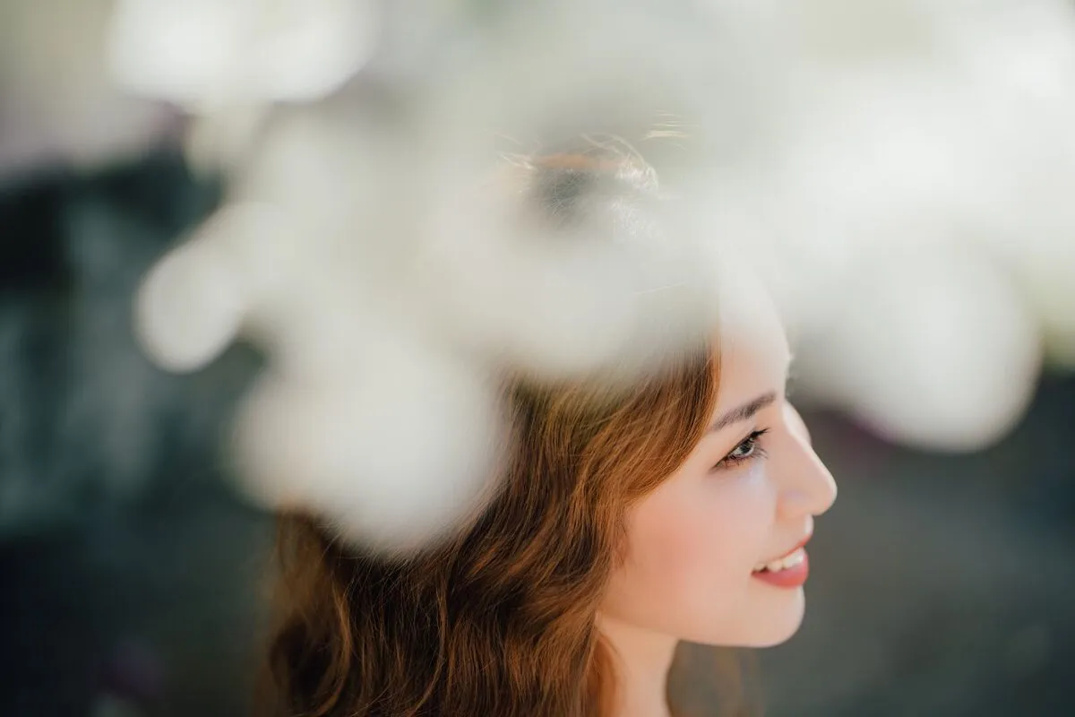 Profile portrait of a smiling woman with out-of-focus white blossoms filling the foreground