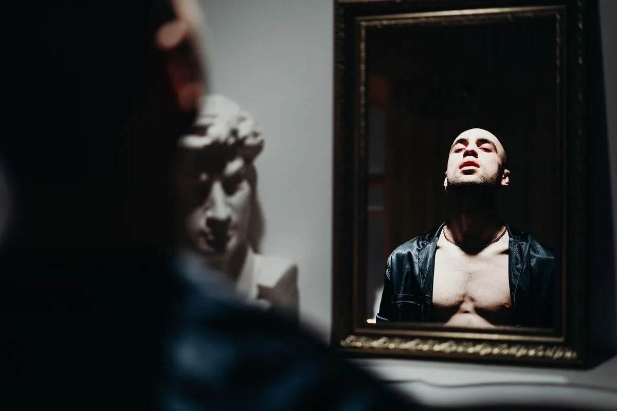 Man's reflection captured inside an ornate gilt mirror, with a blurred classical bust in the foreground
