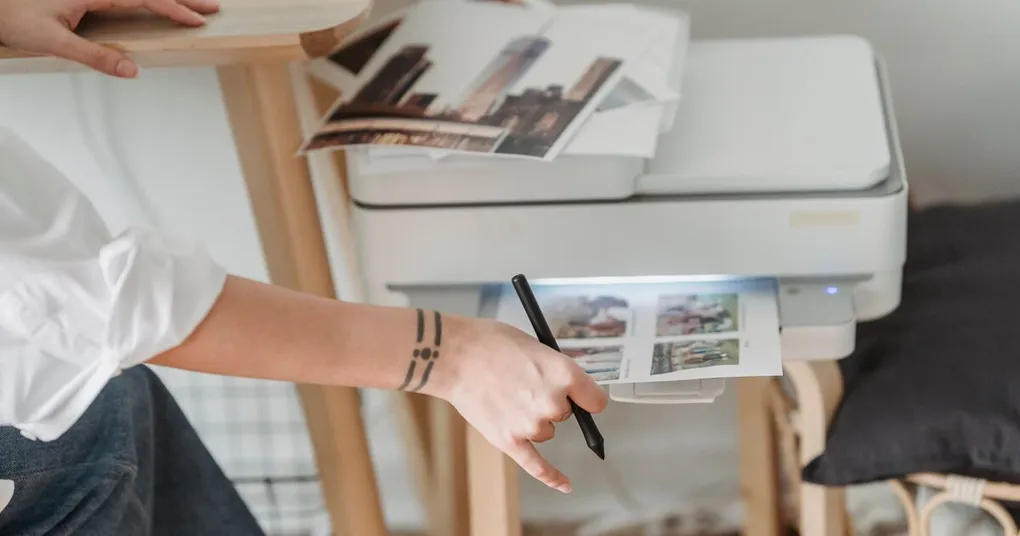 Freshly printed photos emerging from an inkjet printer beside a stack of finished prints