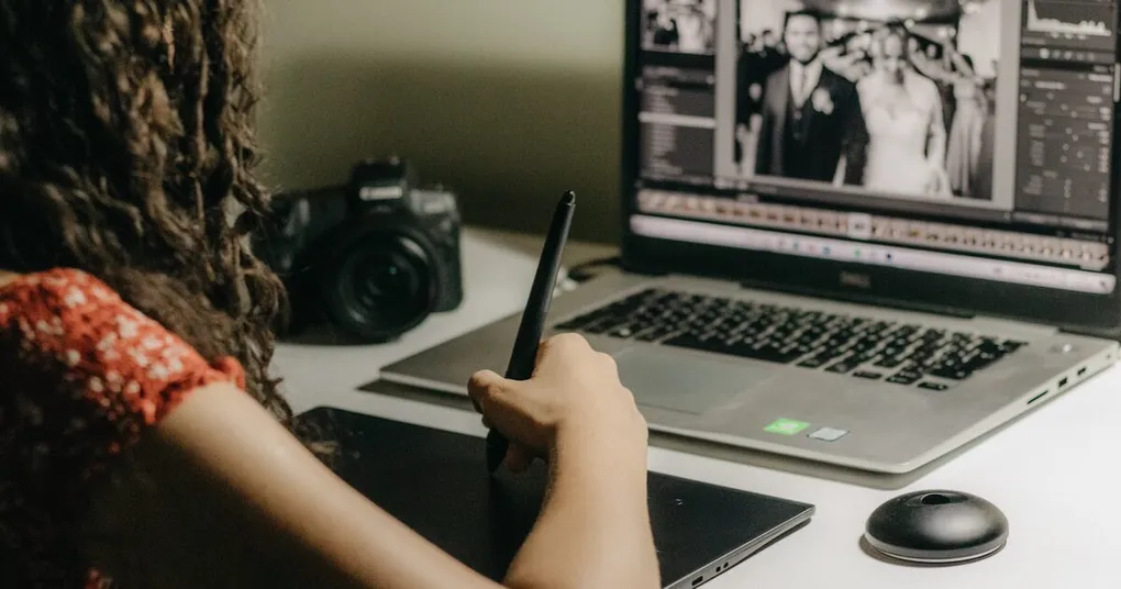 Wedding photographer culling a black and white wedding photo on a laptop, with a camera and graphics tablet on the desk