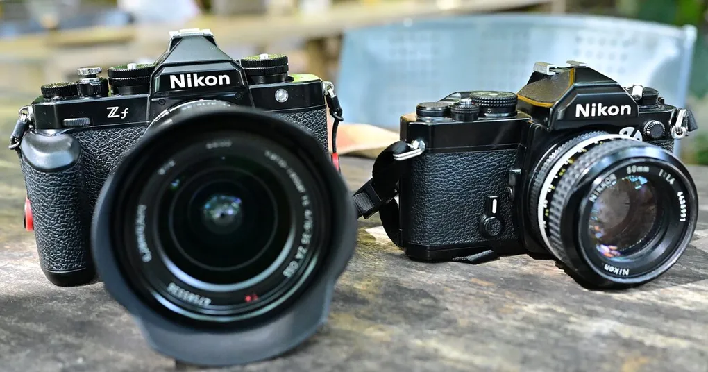Nikon Zf mirrorless camera beside a Nikon film SLR with a Nikkor 50mm f/1.4 lens on a weathered table, the kind of kit whose photos lived on Nikon Image Space