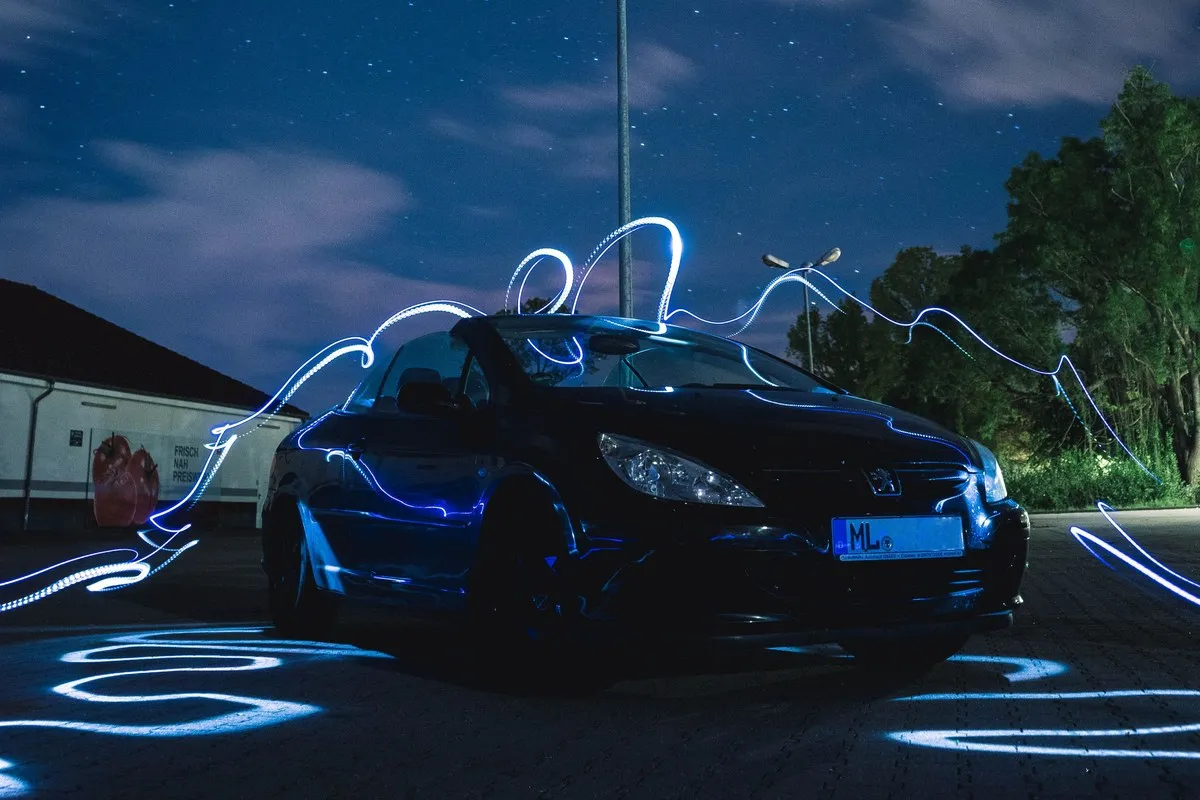 A car surrounded by blue light painting trails under a starlit sky