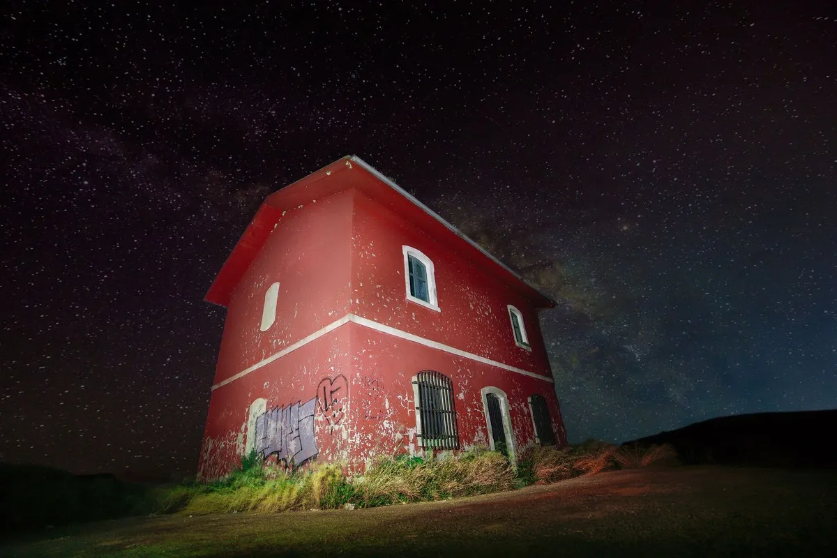 An abandoned red house painted with light under a starry sky