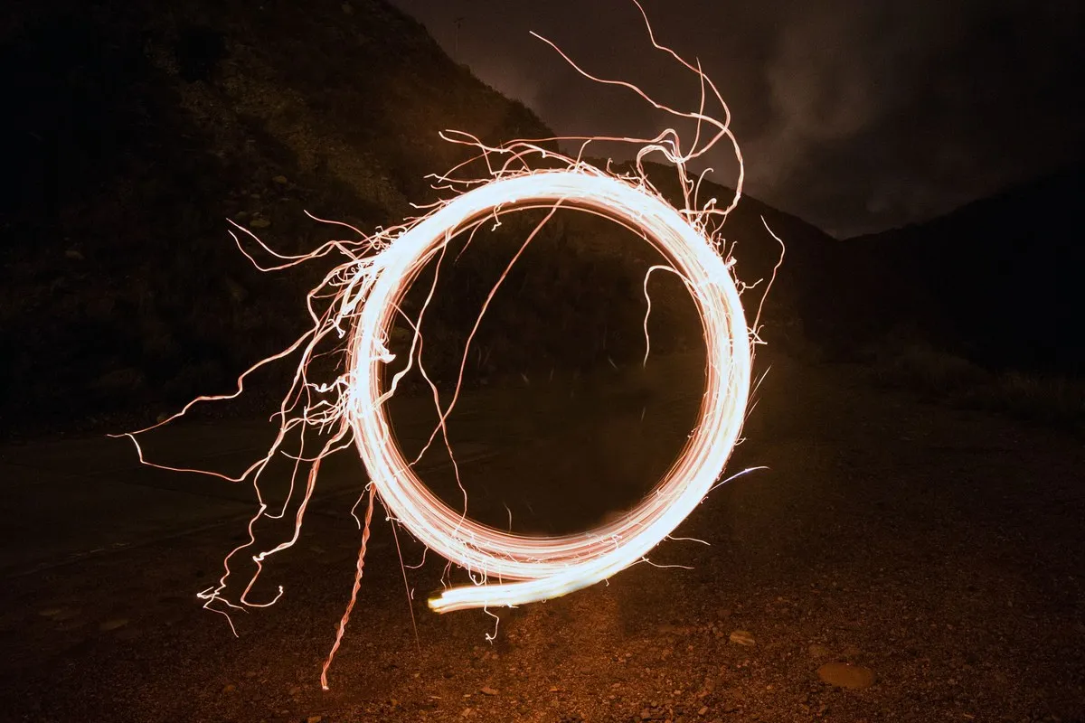 A luminous circle of light spun on a string on dark rocky ground