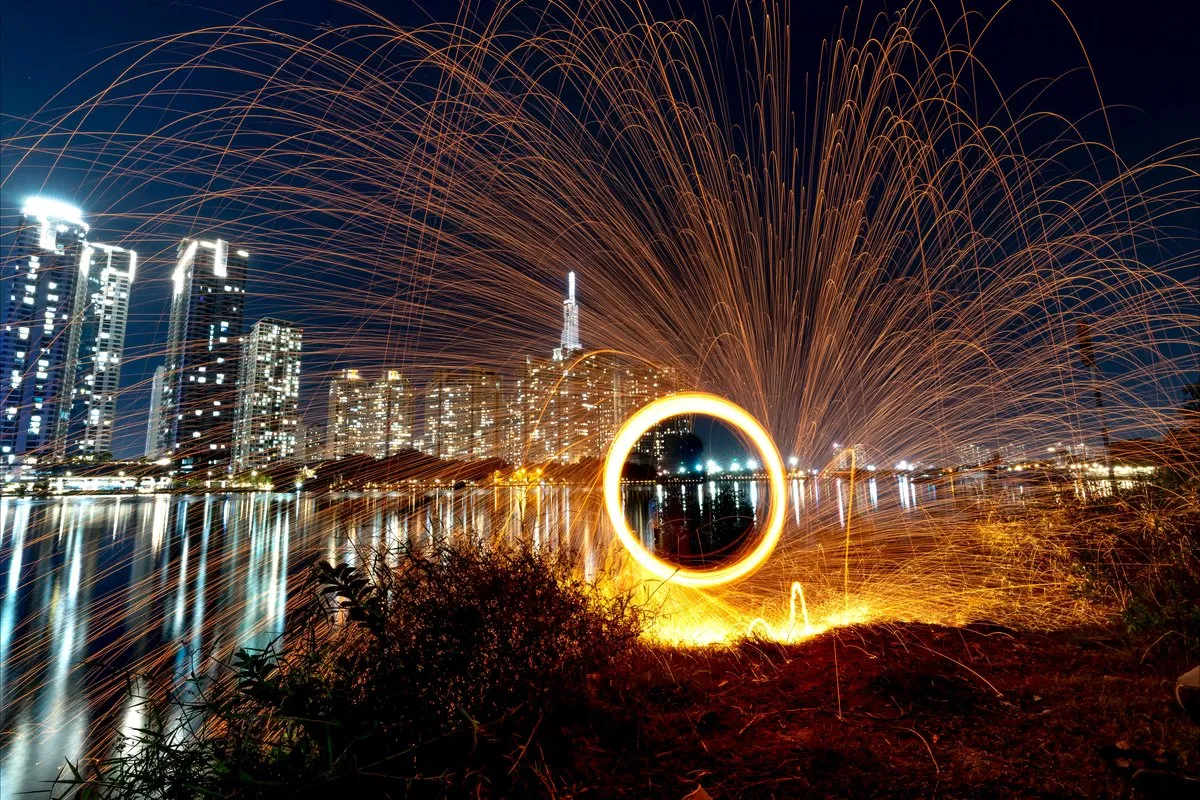 Steel wool spinning sparks over a riverfront skyline at night