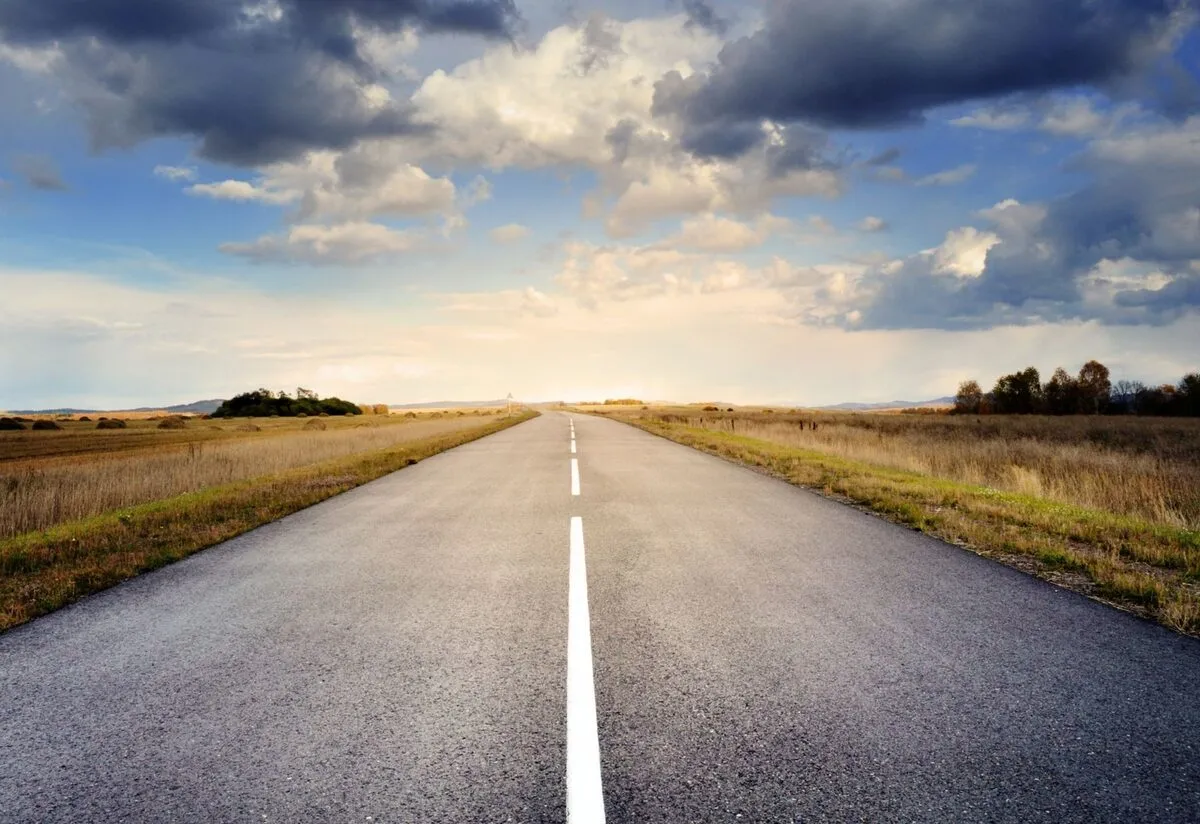 Straight asphalt road with its centre line running to a bright vanishing point on the horizon