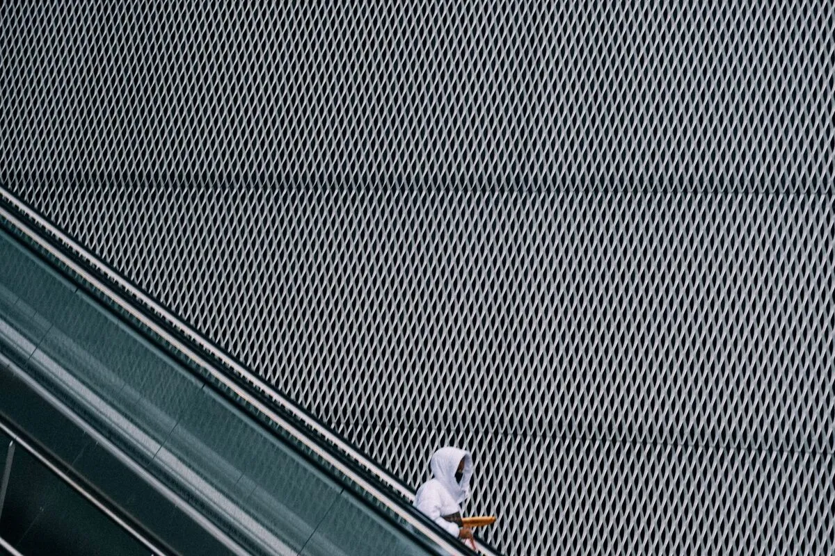 Lone rider on an escalator that cuts diagonally across the frame against a textured metal wall