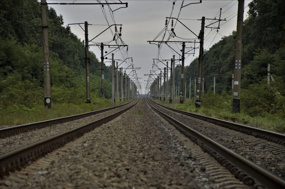 Railway tracks and overhead line poles converging toward a single vanishing point on the horizon