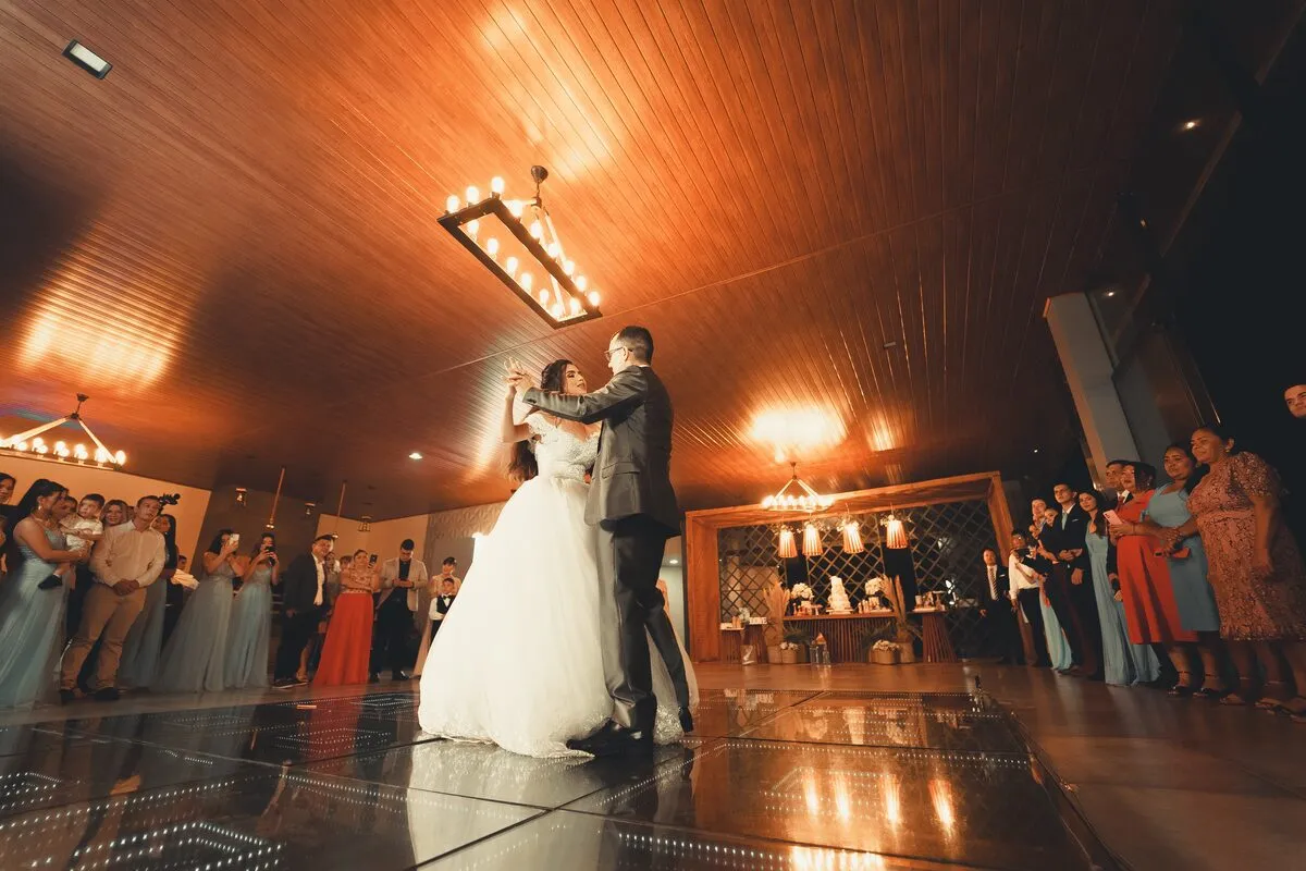 Newlyweds having their first dance on a reception floor as seated guests watch under warm ceiling lights