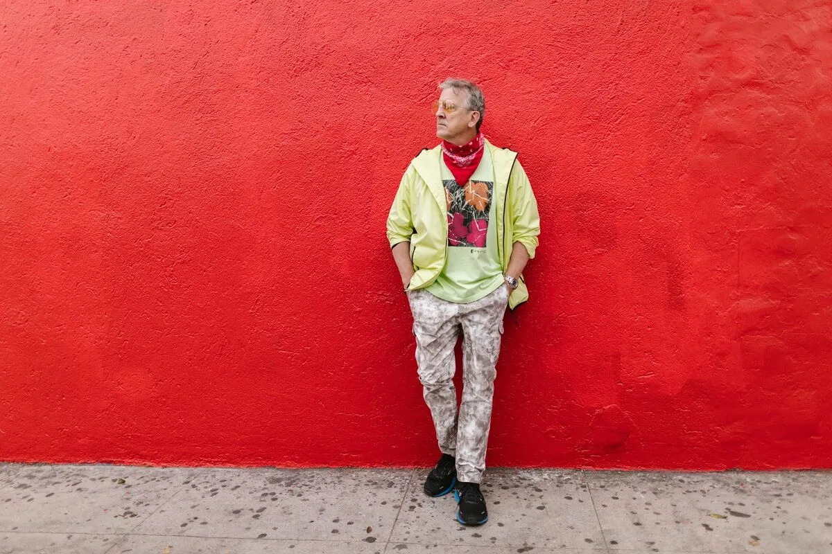 Man in a yellow jacket leaning against a large flat red wall shot square-on