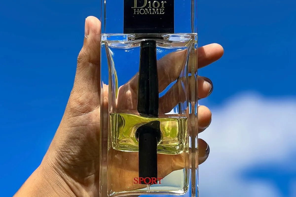 A hand holding a perfume bottle against the sky to show its size