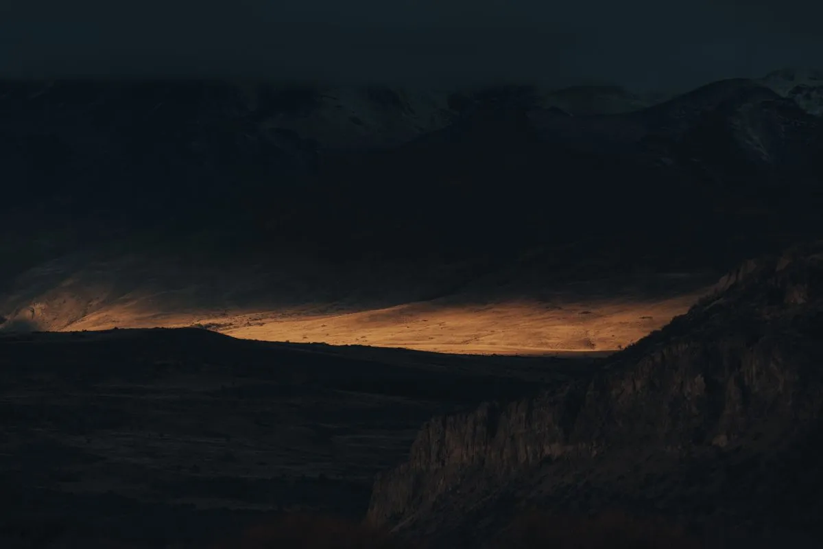 A band of warm golden light striking a valley floor beneath dark, cool-toned mountains