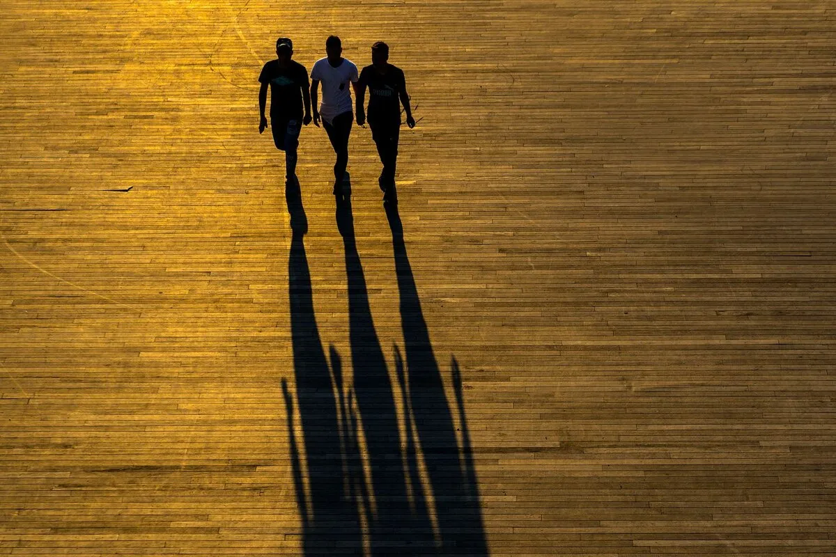 Three people walking at golden hour, their long shadows stretching across a wooden boardwalk