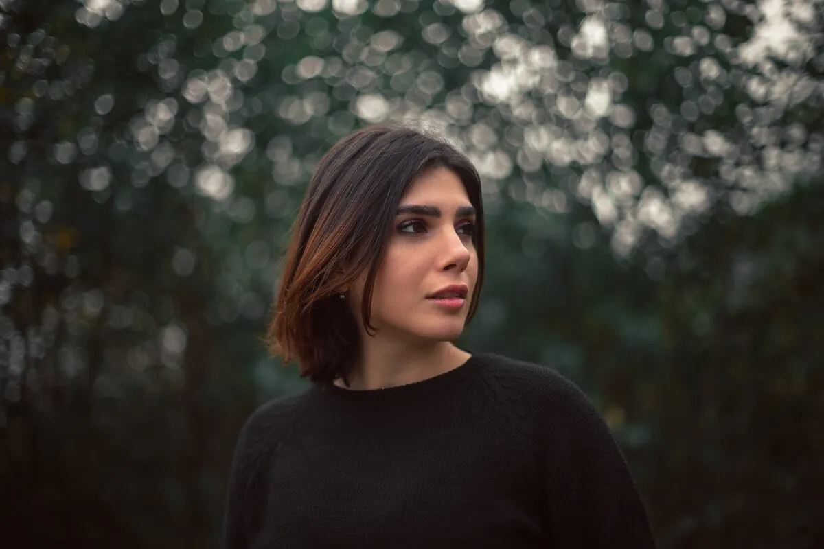 Portrait of a woman in a black sweater against out-of-focus foliage with bright circular bokeh highlights behind her
