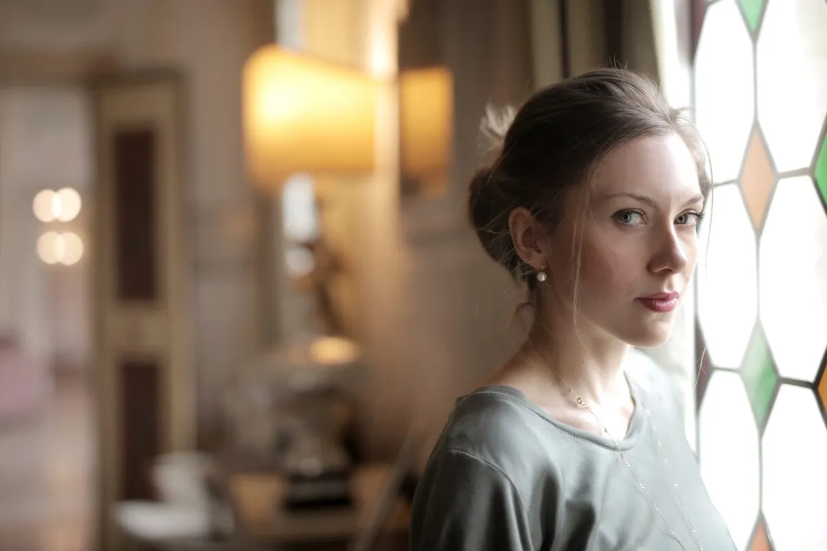 Woman by a stained glass window in a warm interior, lit softly from the side with the room falling away out of focus behind her